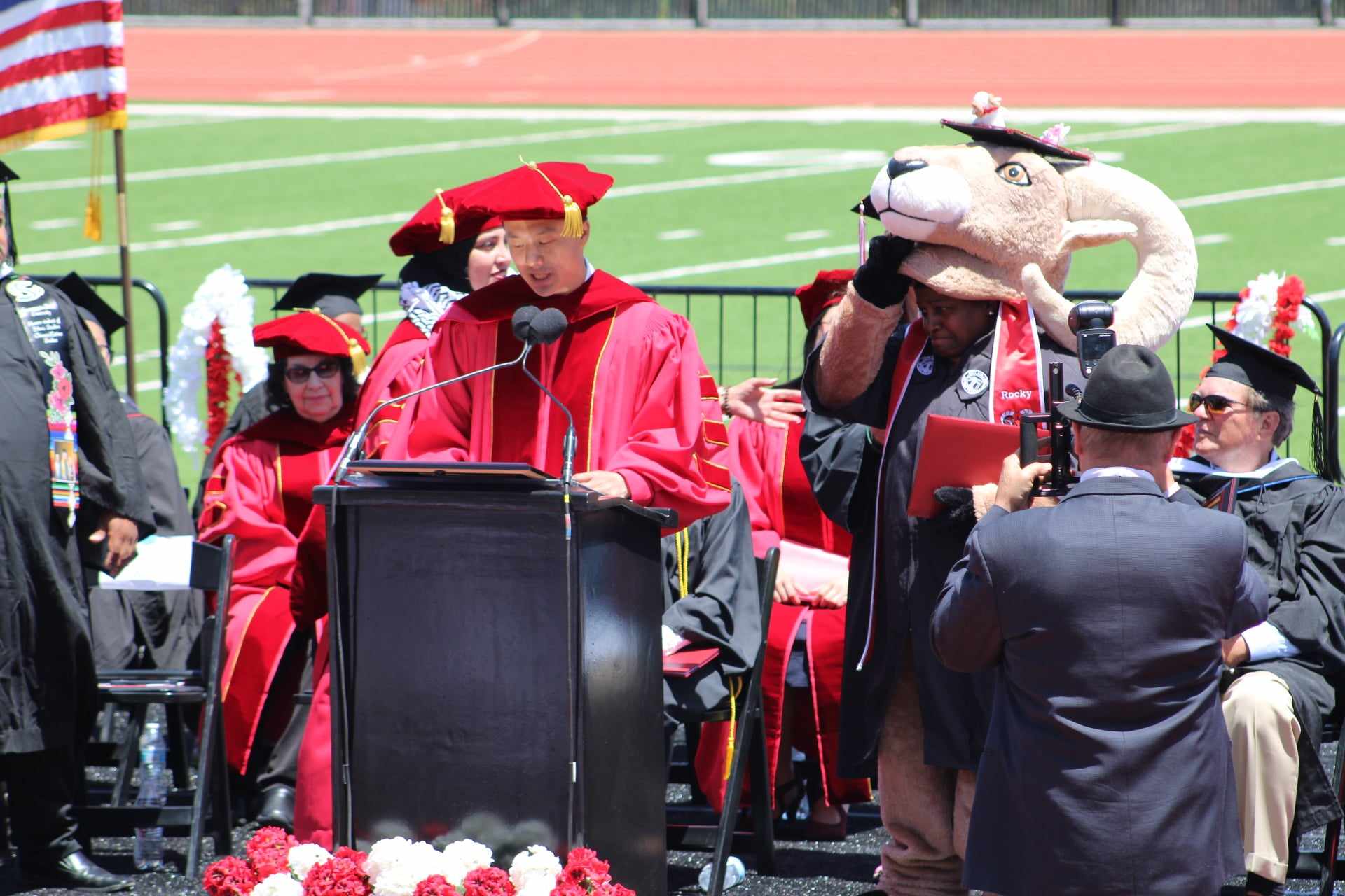 Mascot lifts up mask while on stage at graudation.