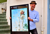 Man holding a painting outside a house
